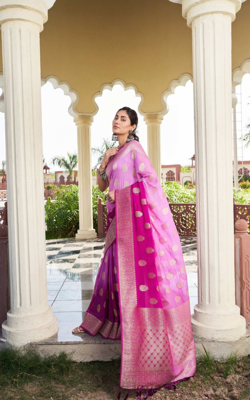 Woman in a pink saree standing in front of classical architecture with columns.