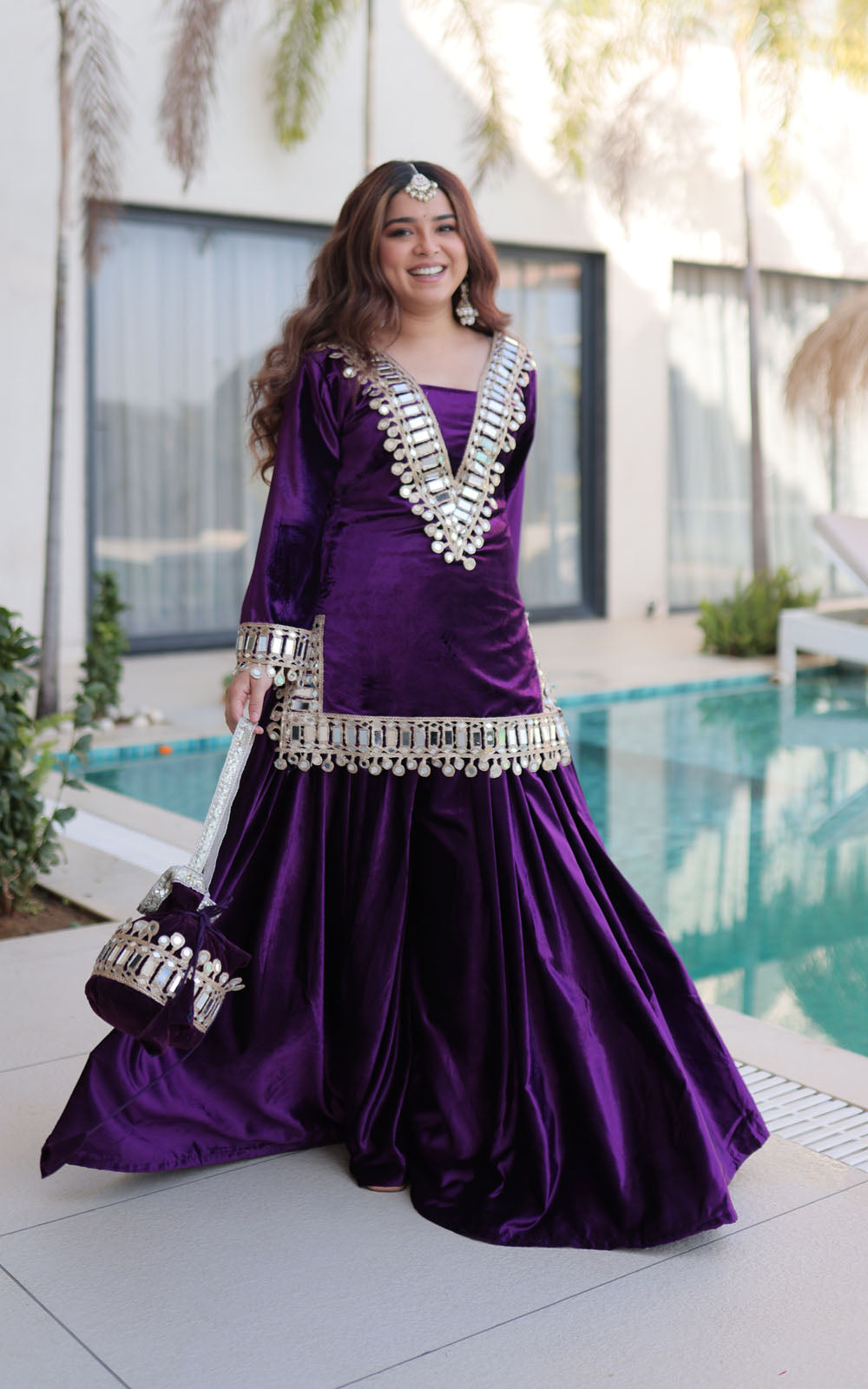 Woman in a purple traditional outfit with silver embellishments standing by a pool.