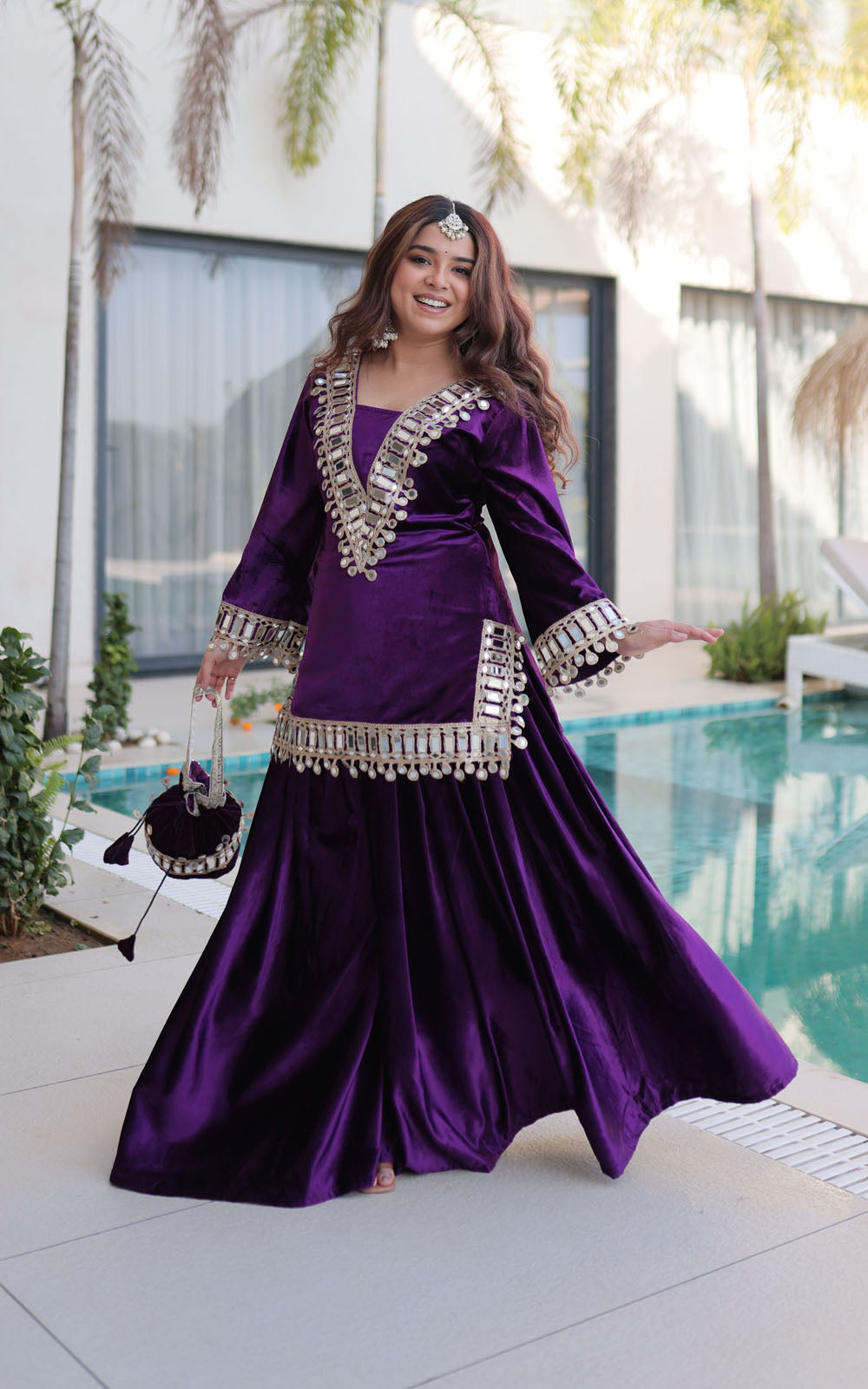 Woman in a purple traditional outfit with silver embellishments by a pool.