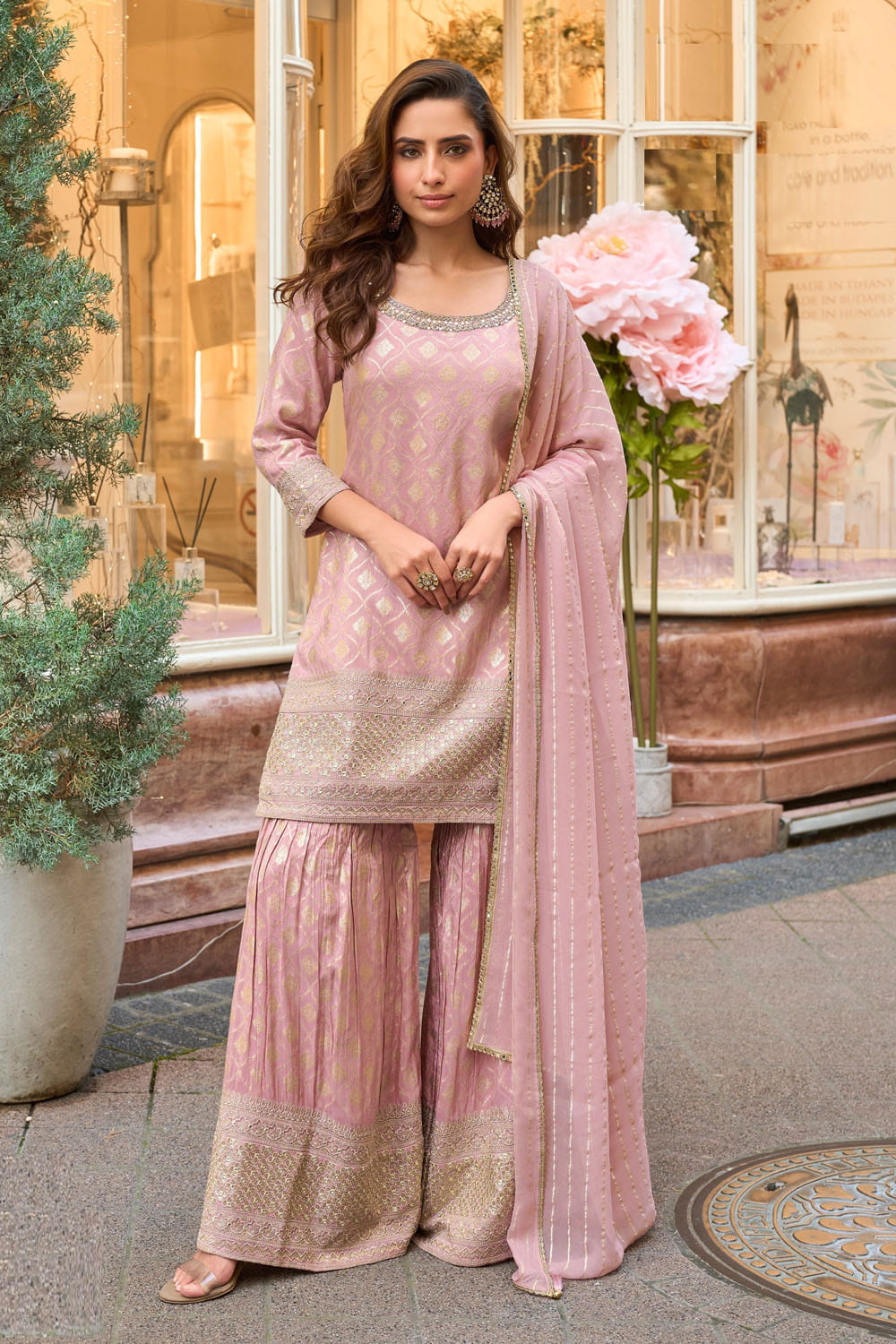 Woman in a pink traditional outfit standing in front of a decorative building entrance.