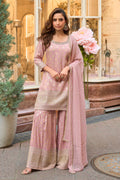 Woman in a pink traditional outfit standing in front of a decorative building entrance.