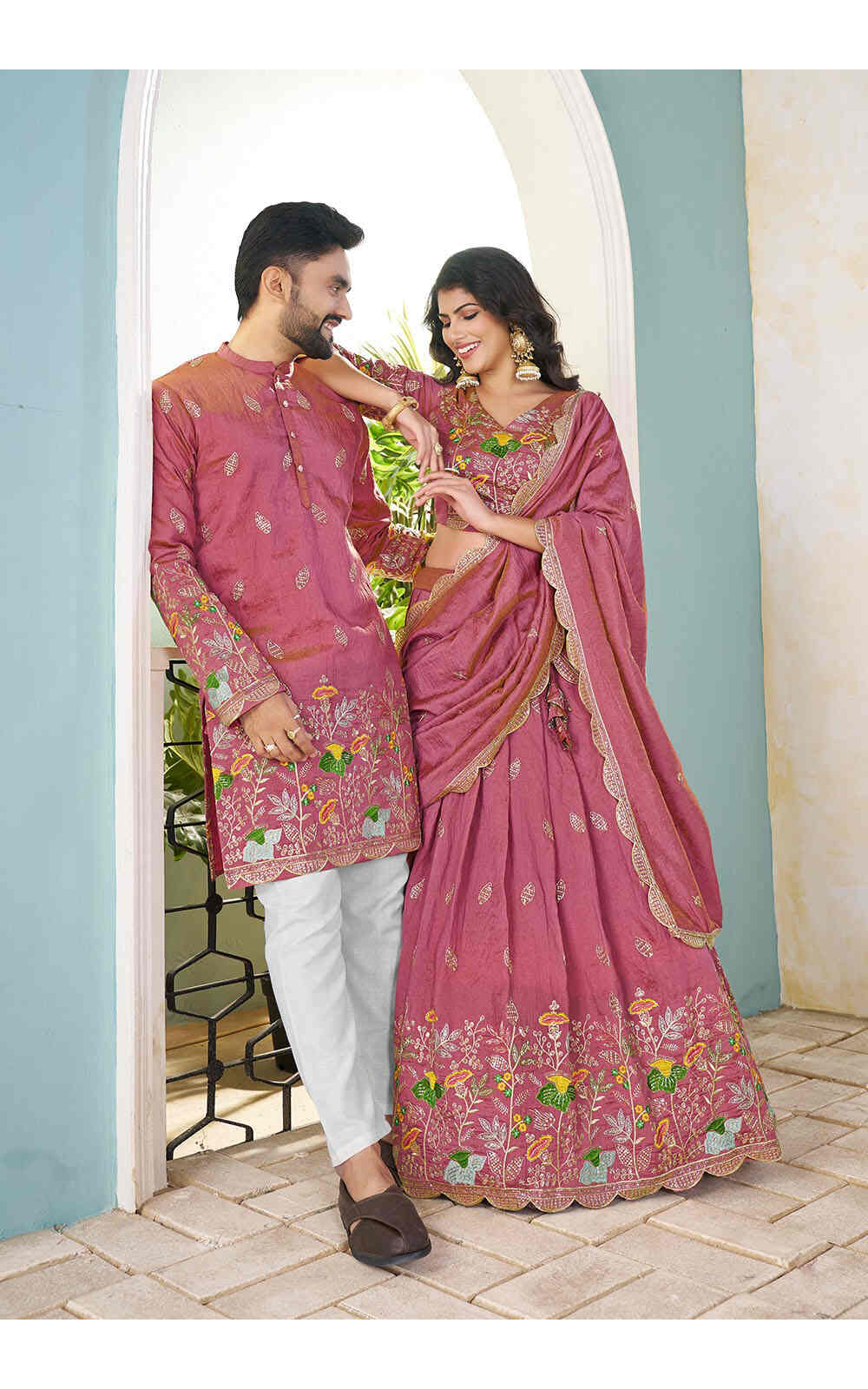Couple in traditional pink embroidered outfits standing in a doorway.