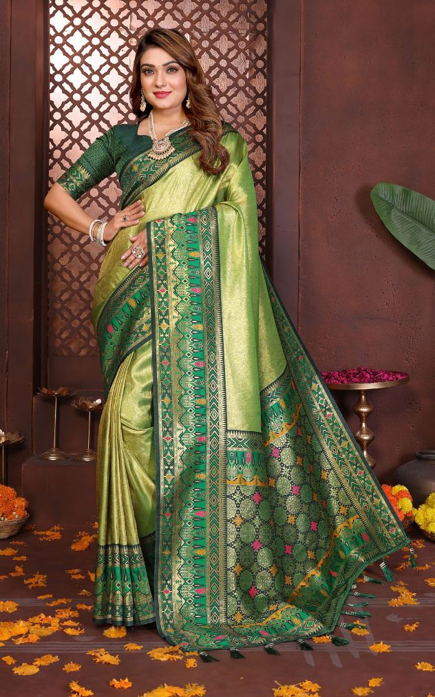 Woman wearing a green and beige saree with intricate patterns on a decorative background.
