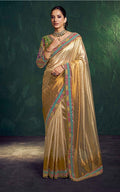 Woman wearing a traditional gold saree with intricate patterns against a dark background