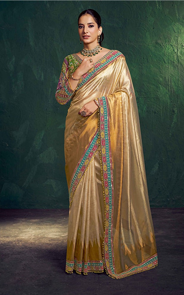 Woman wearing a traditional gold saree with intricate patterns against a dark background