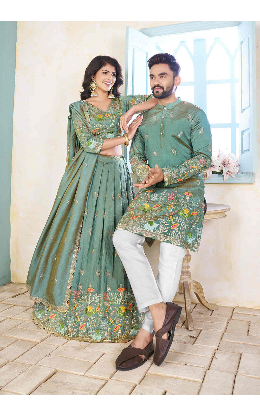 Couple in matching Pista green traditional outfits standing in a room with light blue walls.