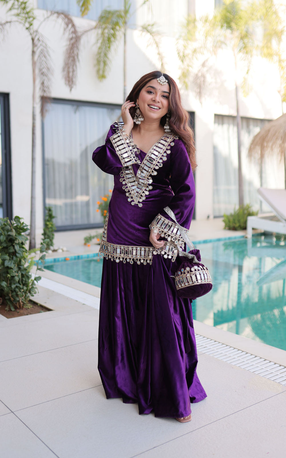 Woman in a purple dress with silver embellishments standing by a pool.