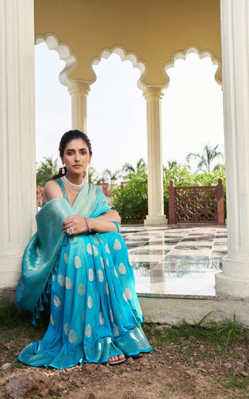 Woman in a blue saree standing in front of an architectural structure with columns.
