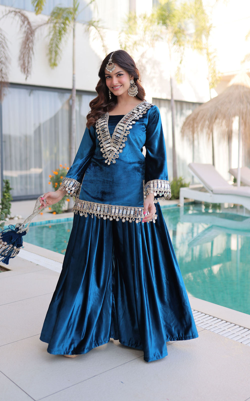 Woman in a blue traditional outfit with silver embellishments by a pool.