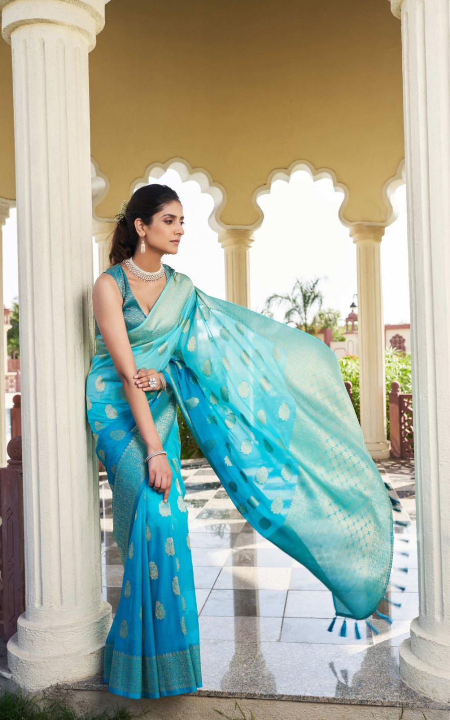 Woman in a blue saree with white patterns standing in front of an architectural structure.
