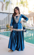 Woman in a blue traditional outfit with silver embellishments standing by a pool.