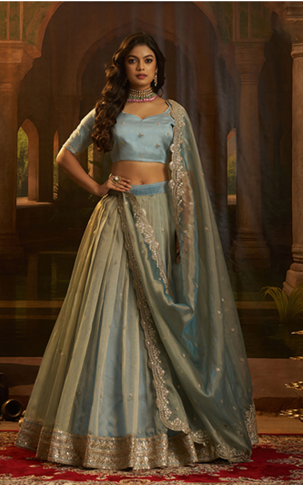 Woman in a traditional outfit with a blue top and green dupatta in an ornate setting