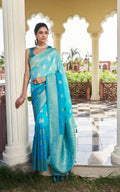 Woman in a blue saree standing in front of a decorative archway with a garden view.