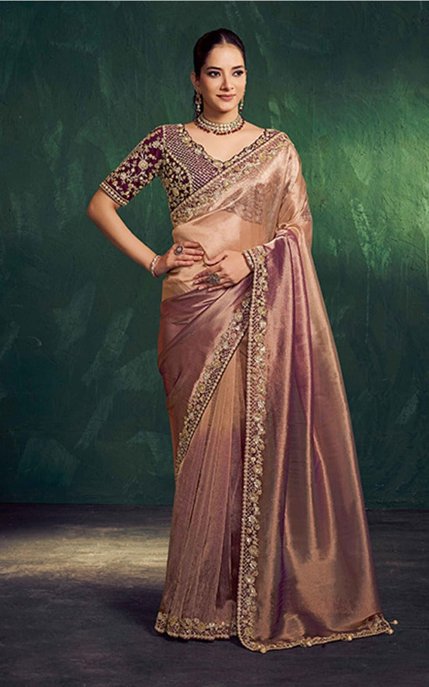 Woman wearing a beige saree with intricate designs against a dark green background