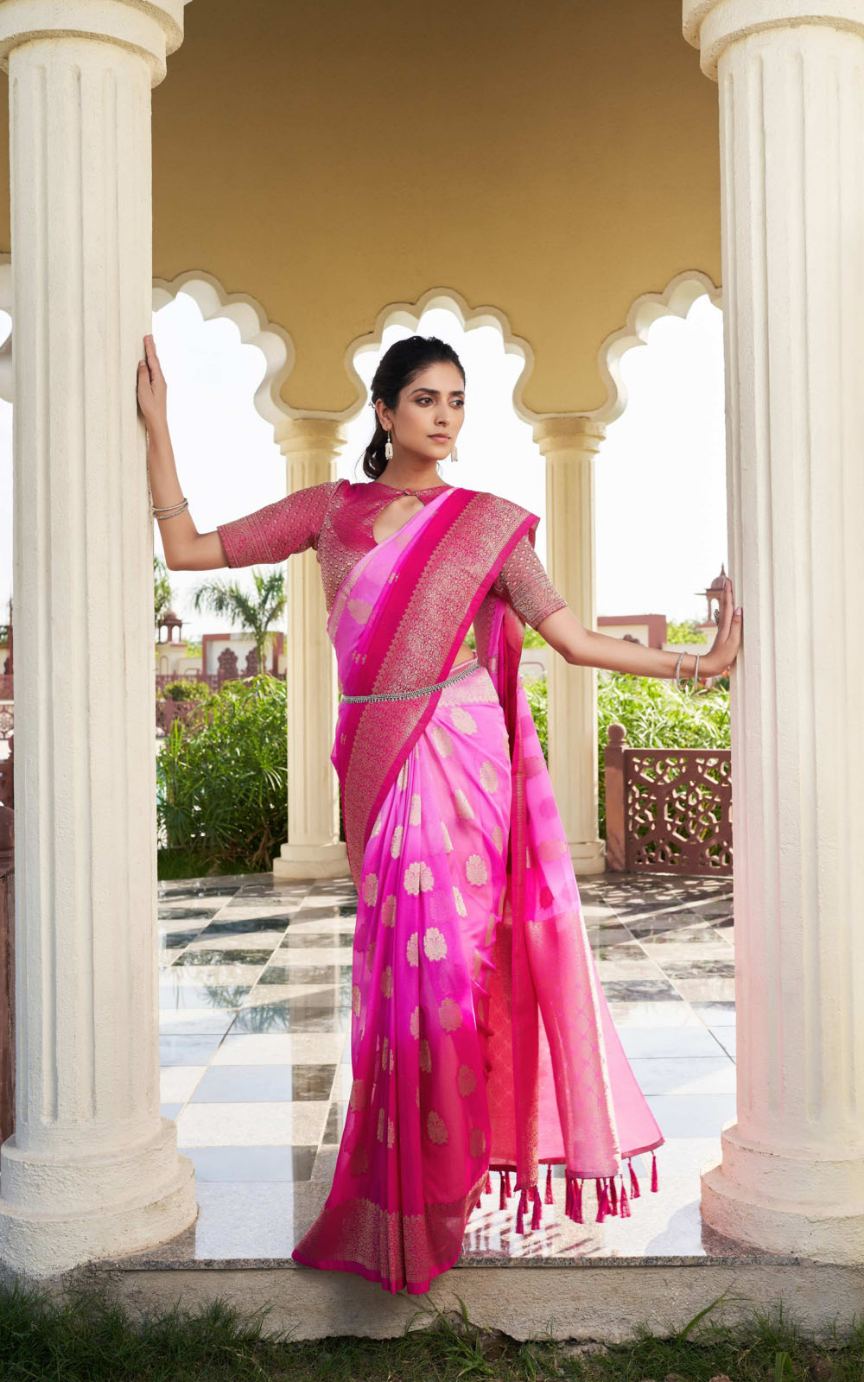 Woman in a pink saree standing between two columns with a garden view.