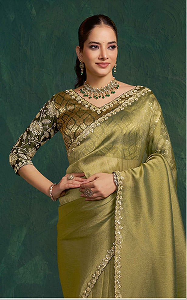 Woman wearing a green saree with intricate designs against a dark green background