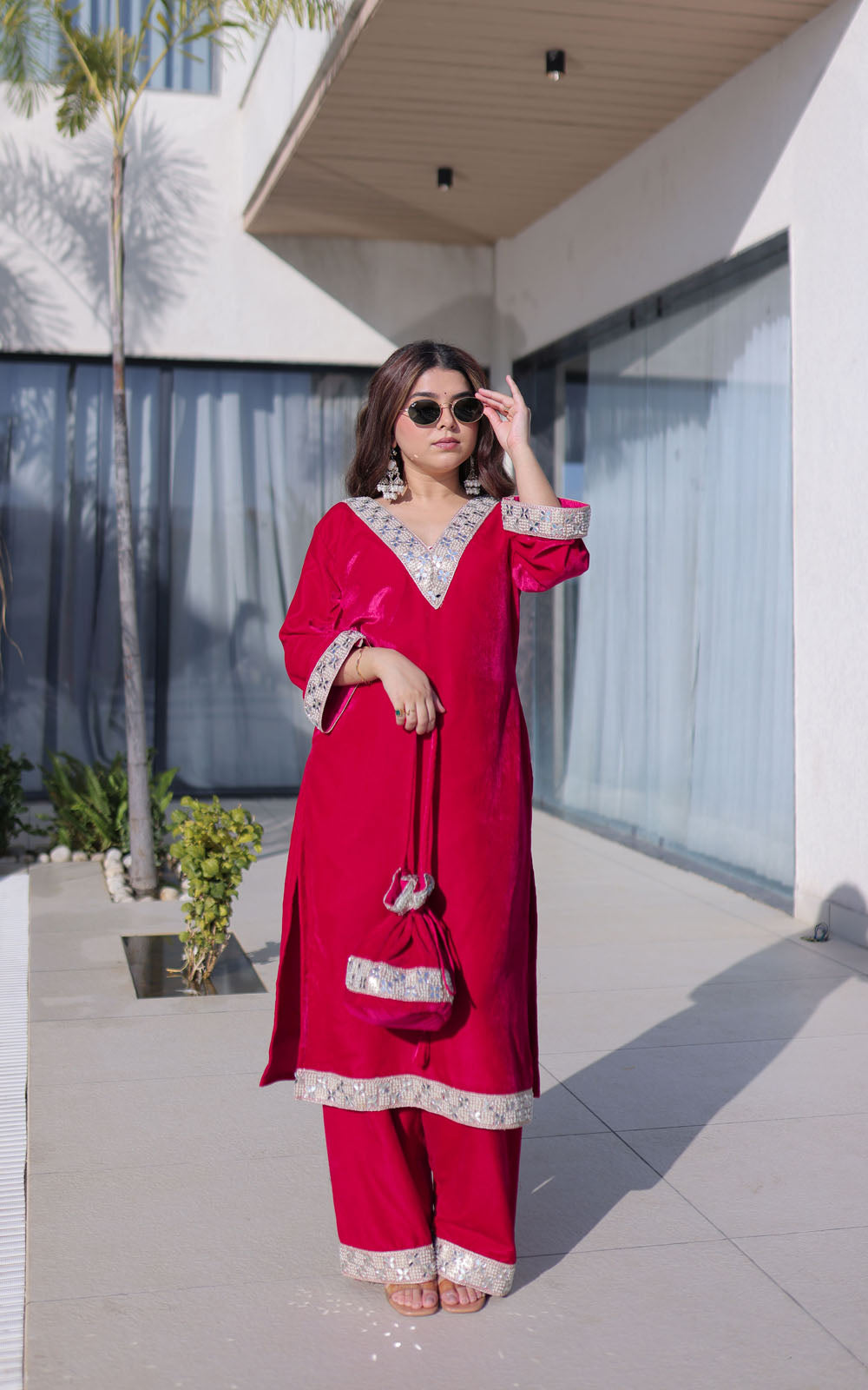 Woman in a red traditional outfit standing outdoors near a modern building.