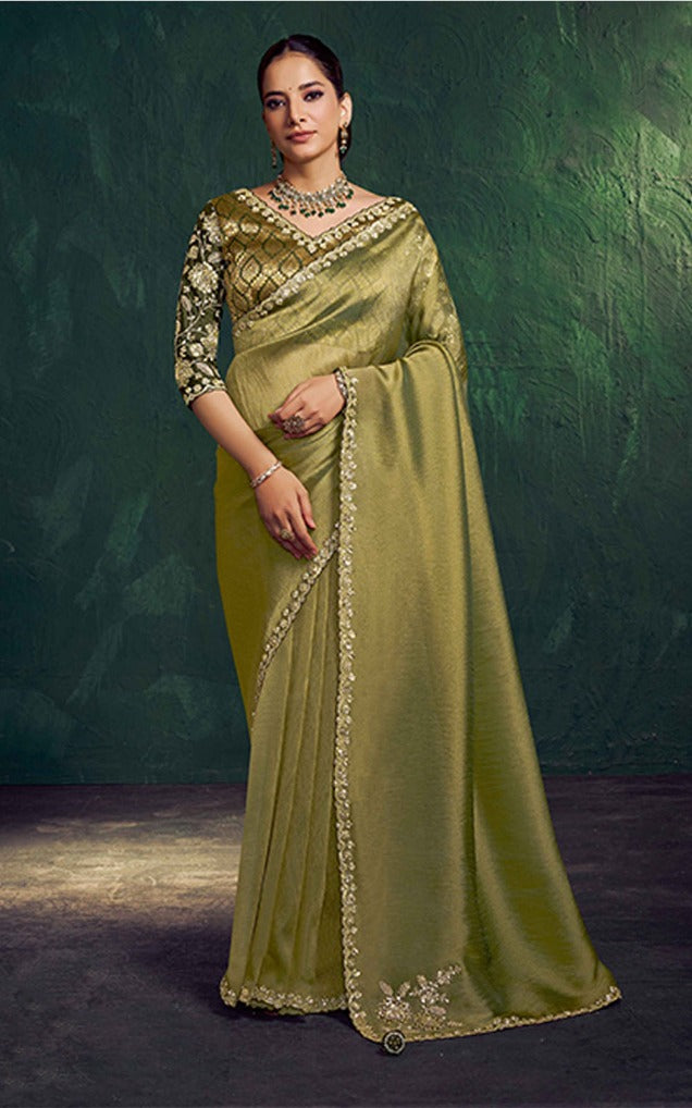 Woman wearing a green saree with gold embroidery against a dark background