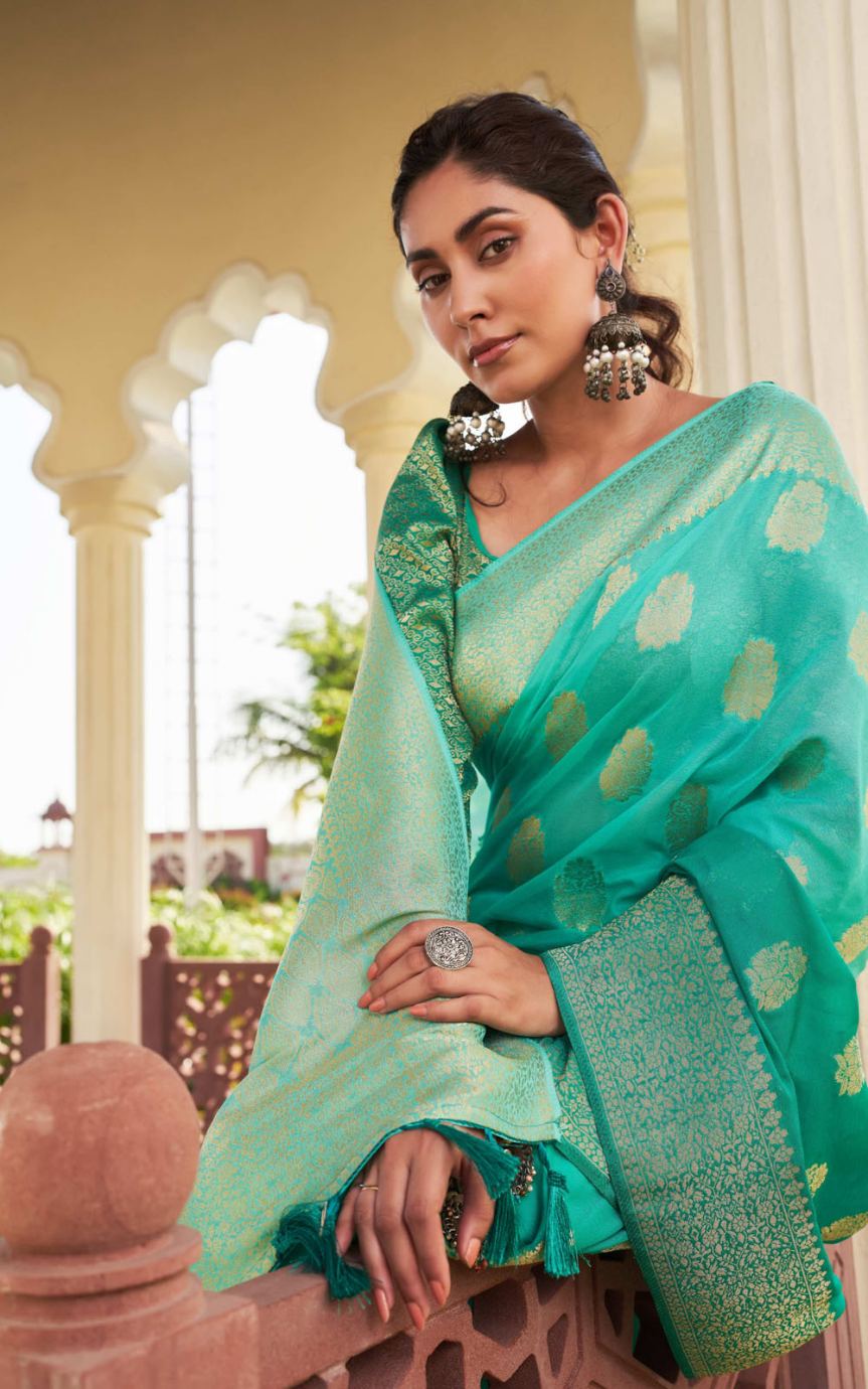 Woman wearing a green saree with a polka dot pattern, standing in an outdoor setting.