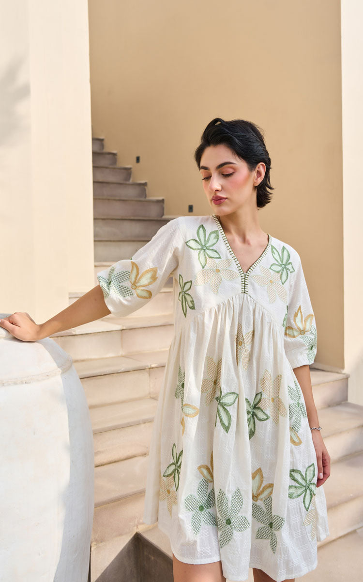 Woman in a white dress with green floral patterns standing on a staircase.
