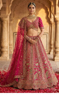 Woman in traditional pink and gold embroidered outfit with a long train, standing in an architectural setting.