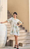 Woman in a light-colored dress with floral patterns standing on stone steps.