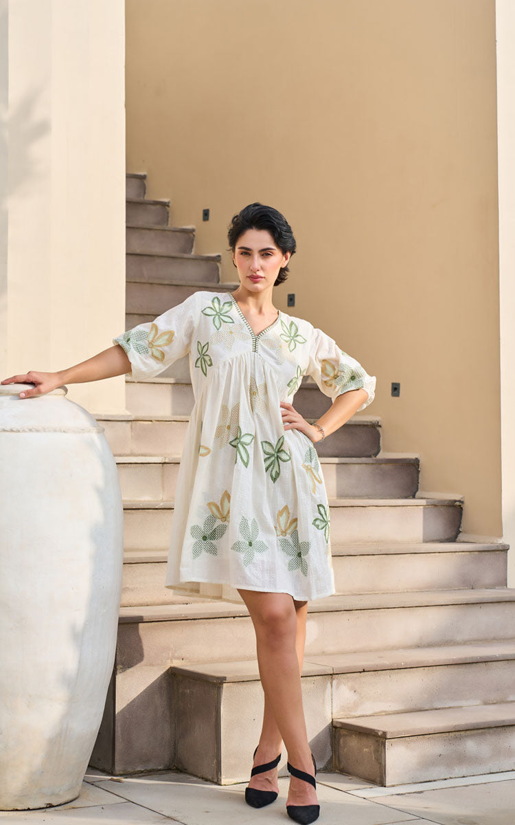Woman in a light-colored dress with floral patterns standing on stone steps.