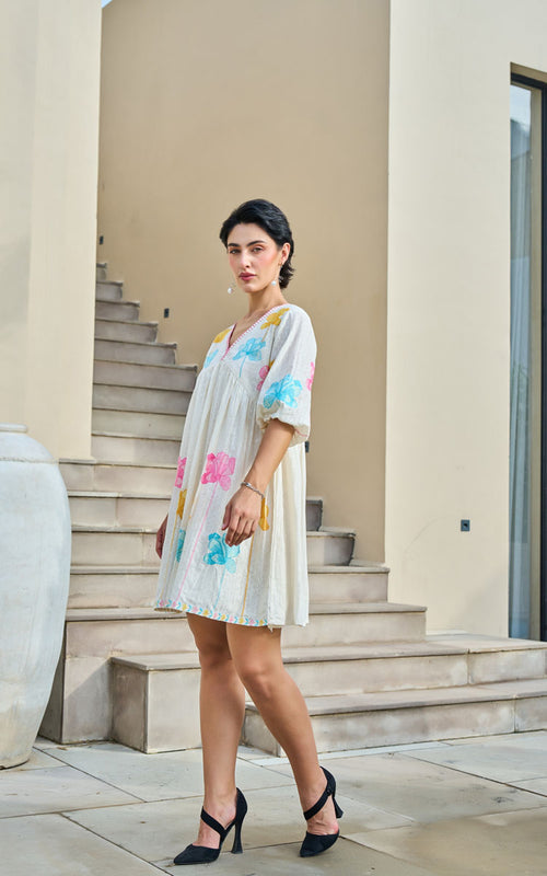 Woman in a white dress with colorful floral patterns standing on steps outdoors.