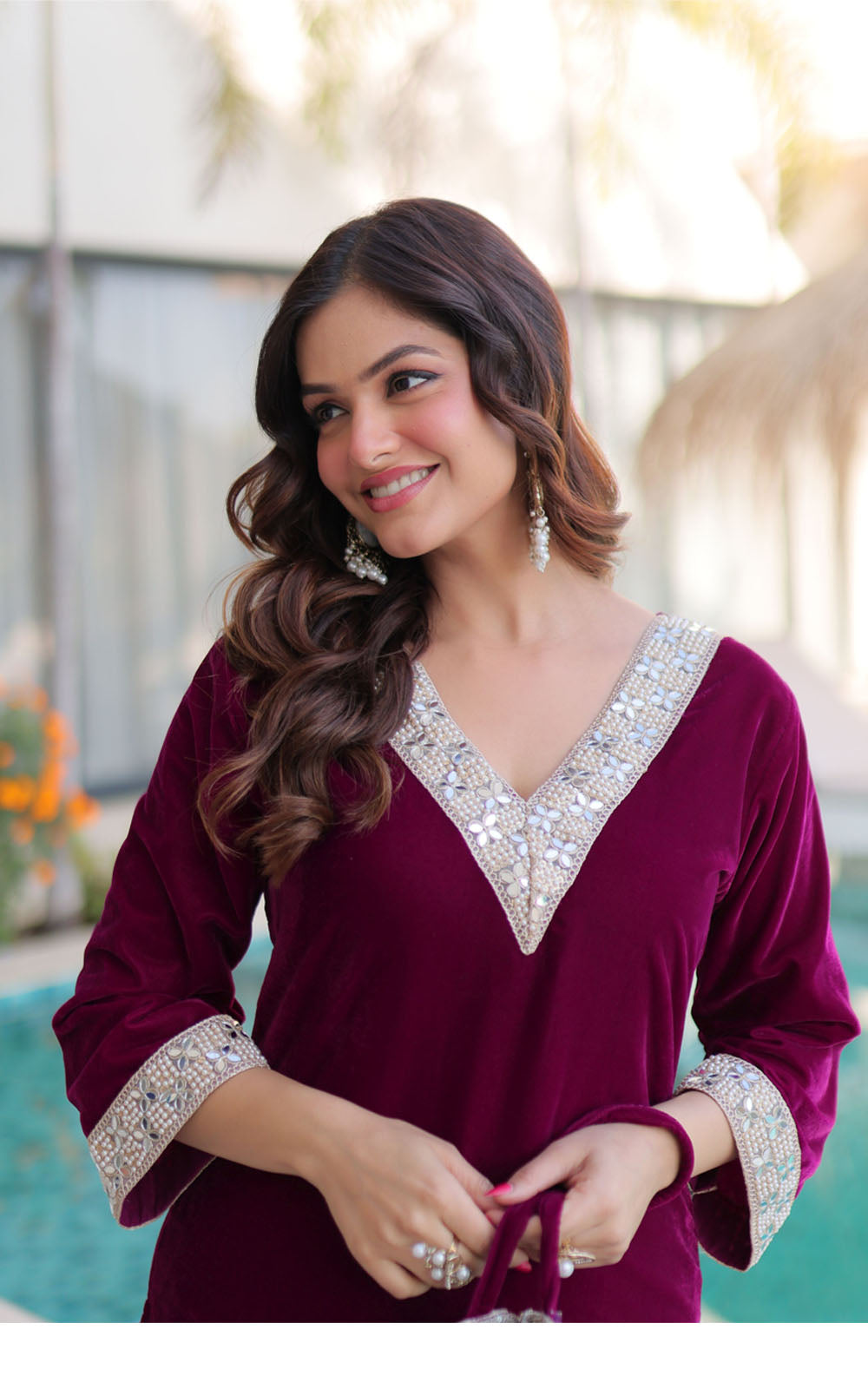 Woman wearing a burgundy outfit with silver embellishments by a pool.