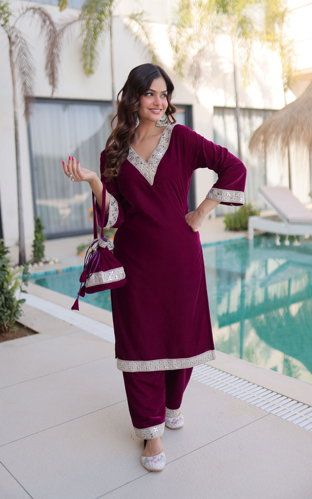 Woman in a maroon traditional outfit with white patterns standing by a pool.