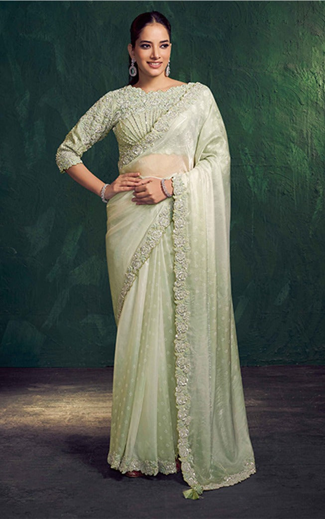Woman wearing a light green saree with a dark green background
