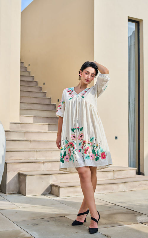 Woman in a white dress with floral embroidery standing on steps outdoors.