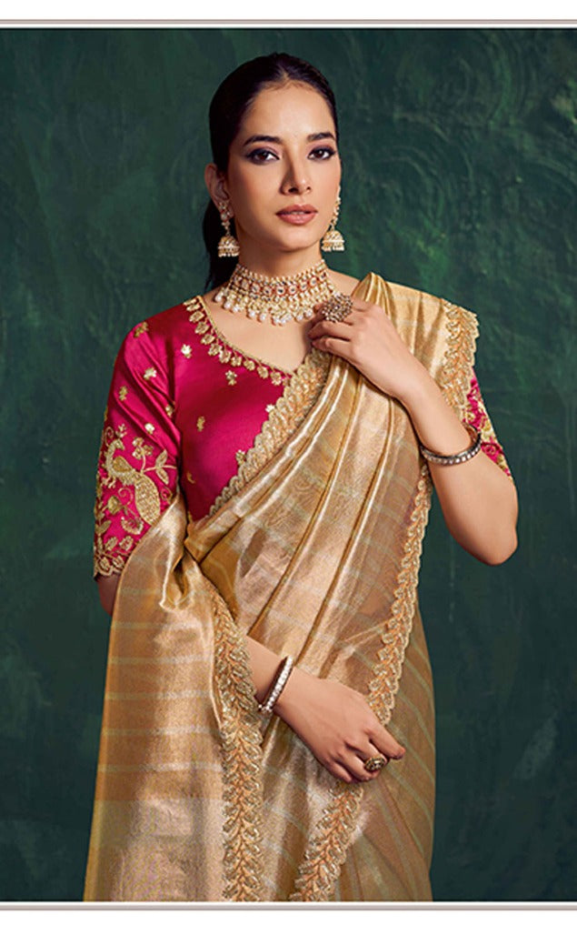 Woman wearing a traditional gold saree with a pink blouse against a green background