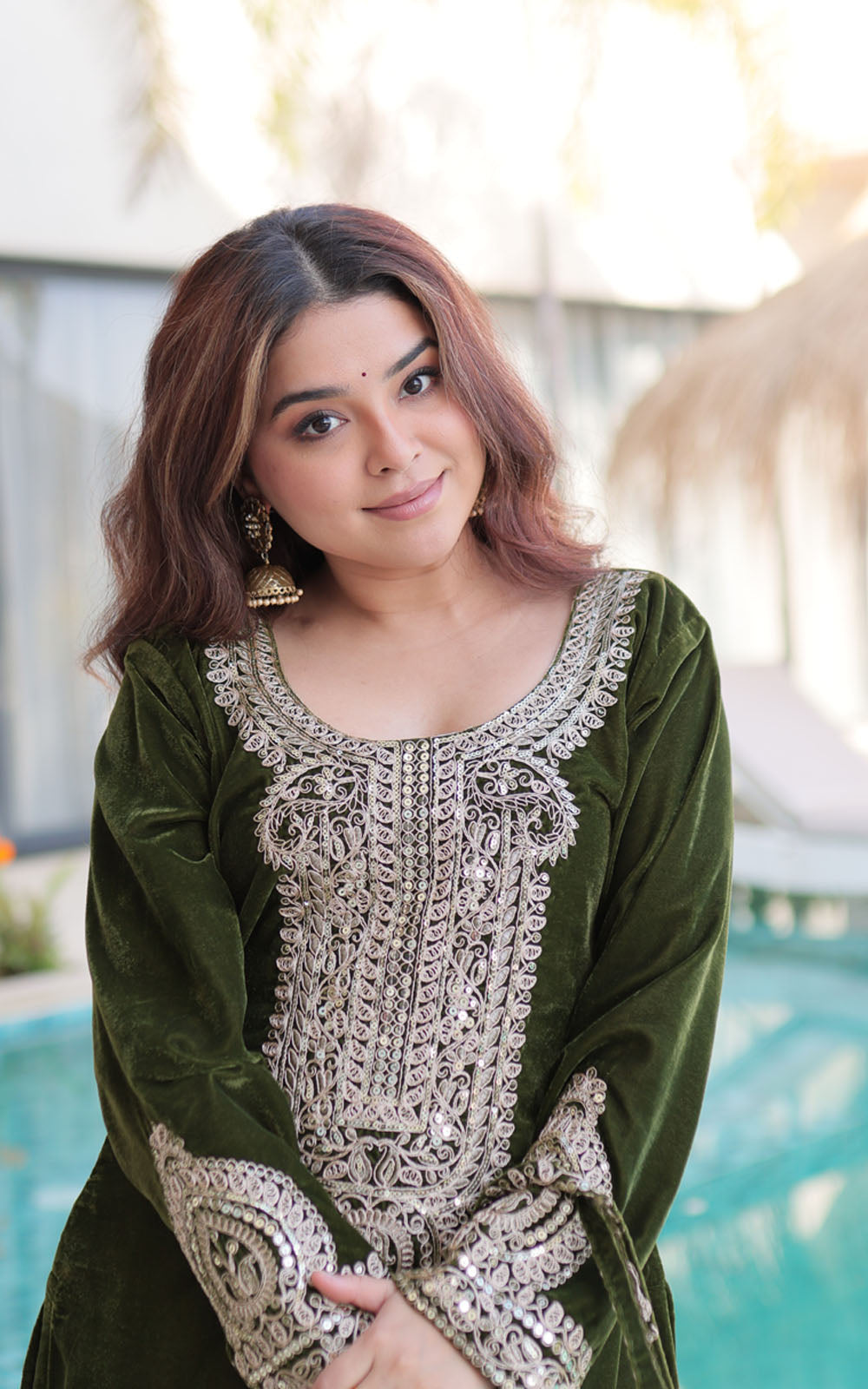 Woman wearing a green traditional outfit with intricate white embroidery, standing by a pool.