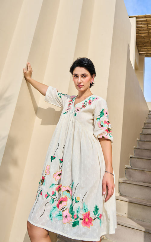 Woman wearing a floral dress standing in front of a beige wall with a staircase.