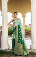 Woman in a green saree with white patterns standing in front of classical architecture.