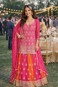 Woman in a pink and orange traditional outfit at an outdoor event with string lights.