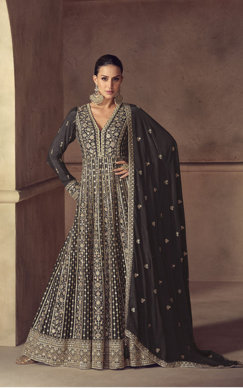 Woman wearing a black and silver embroidered traditional outfit with a cape against a brown wall.