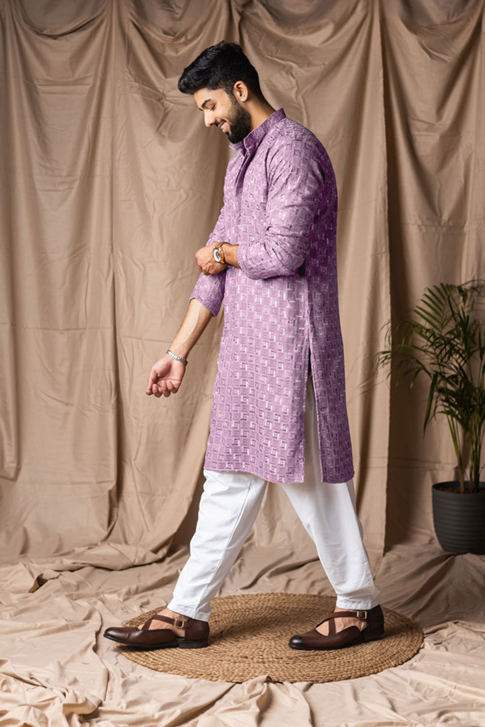 Man wearing a purple kurta with white pants against a beige curtain background