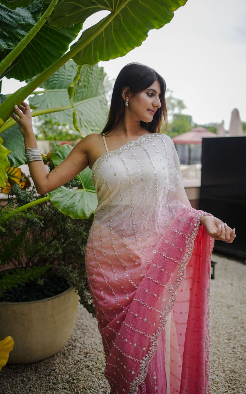 Woman in a white and pink saree standing outdoors with large green leaves in the background