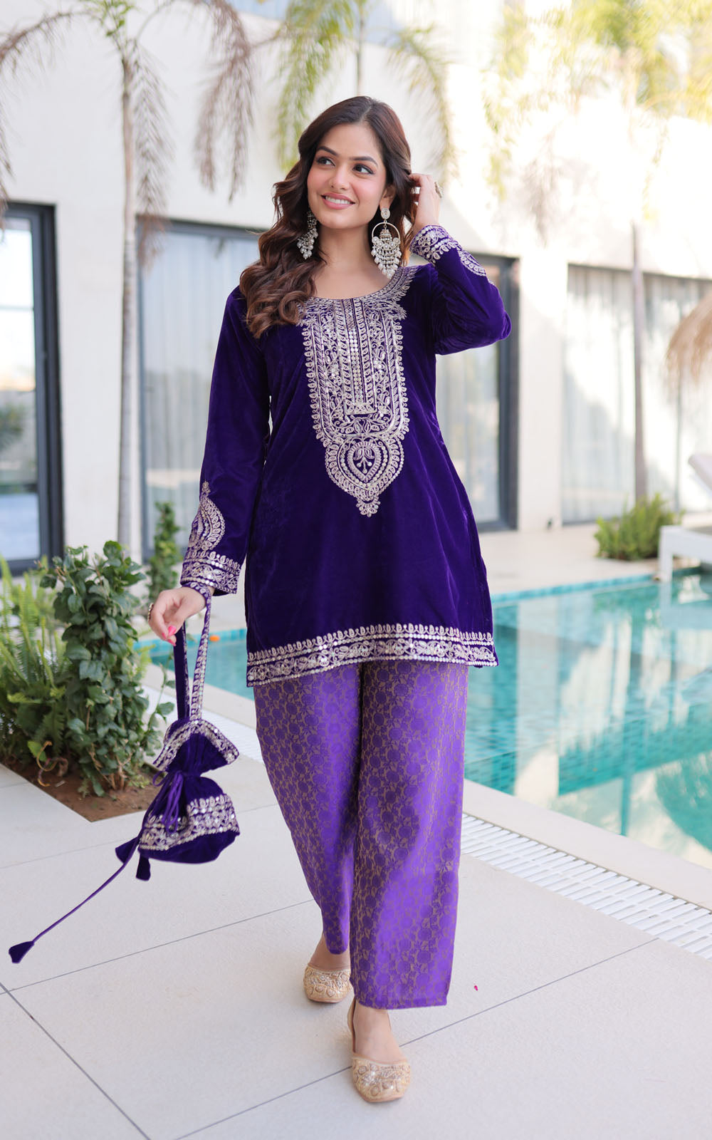 Woman in a purple traditional outfit with white embroidery standing by a pool.