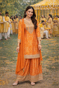 Woman in an orange traditional outfit standing outdoors with a festive background