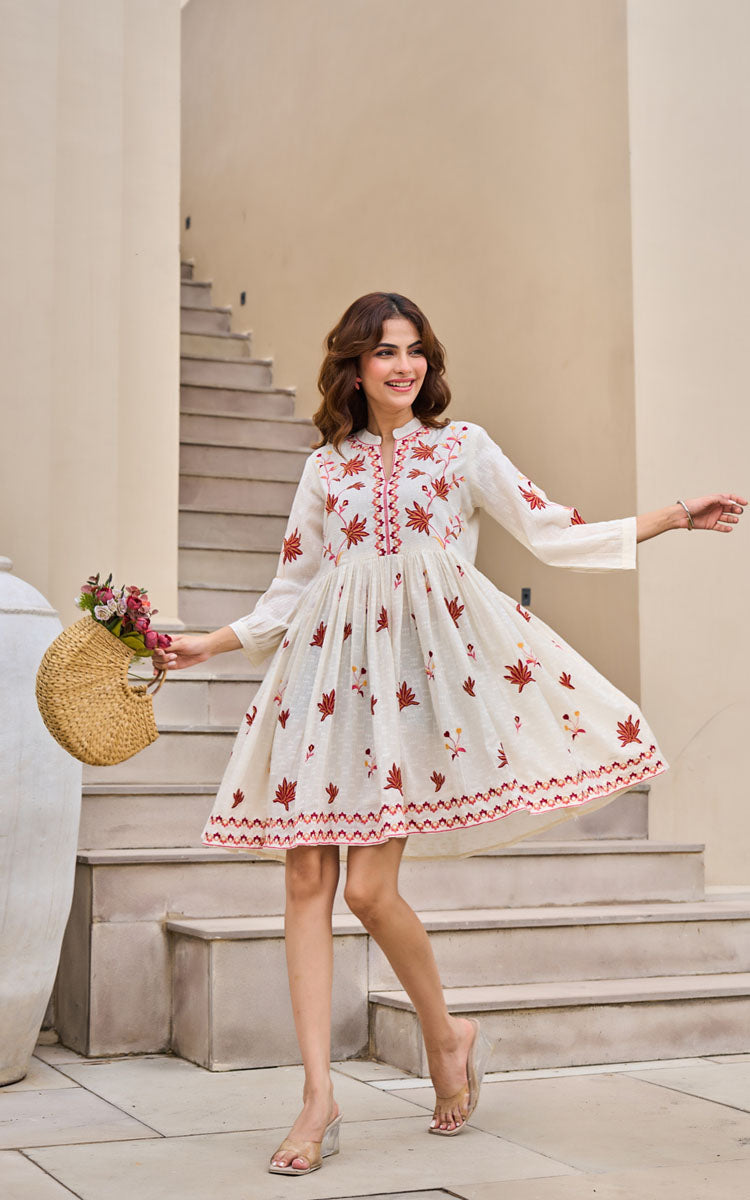 Woman in a white dress with red floral patterns standing on stone steps.