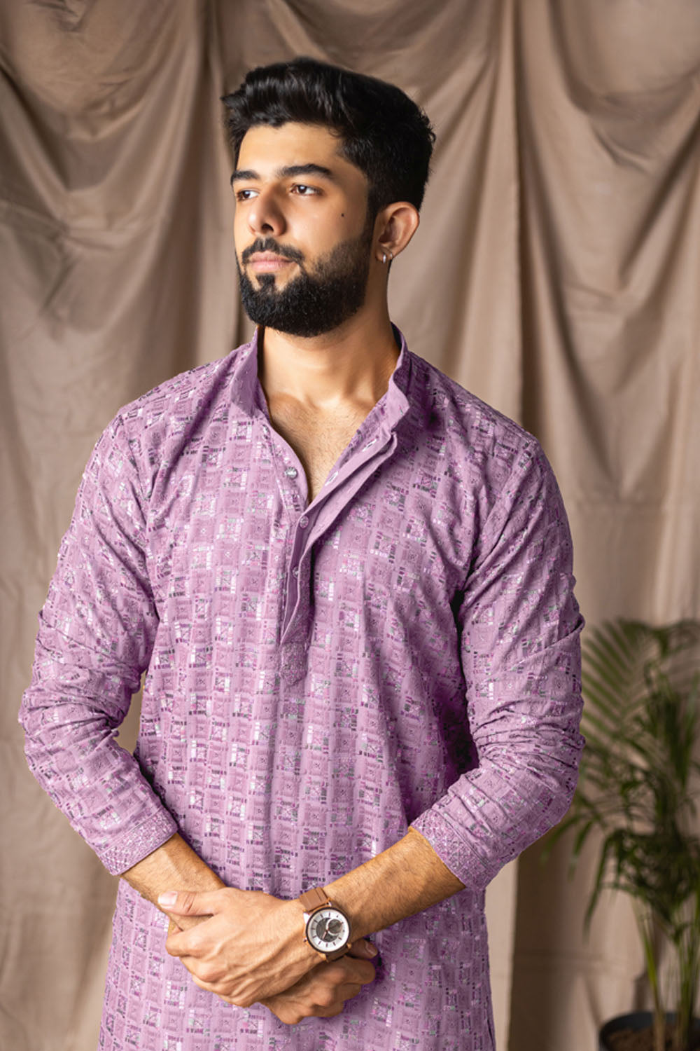 Man wearing a purple patterned shirt against a beige curtain background