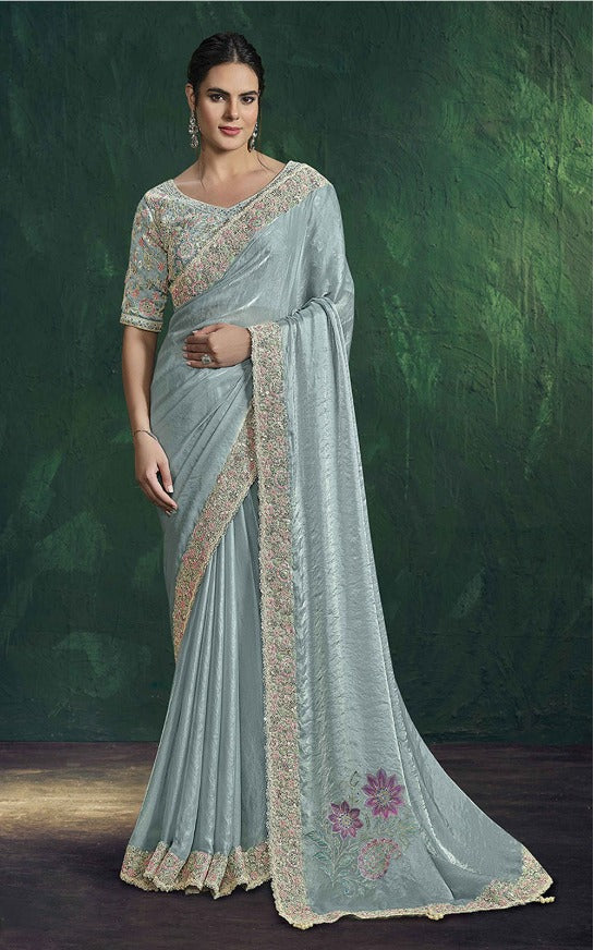 Woman wearing a light blue saree with gold embroidery against a dark green background