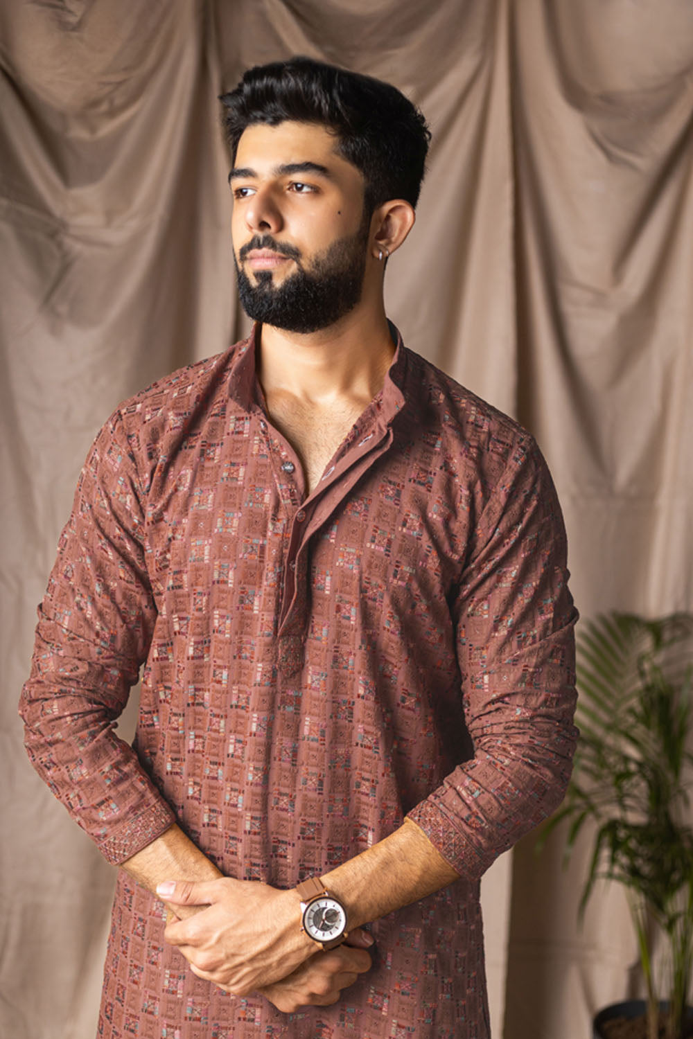 Man wearing a patterned brown shirt against a beige curtain background