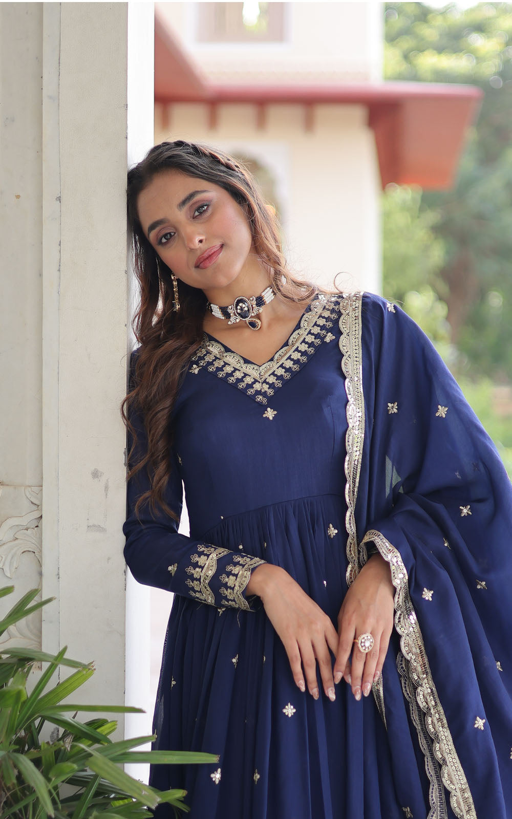 Woman in a blue traditional outfit with intricate designs, standing outdoors.