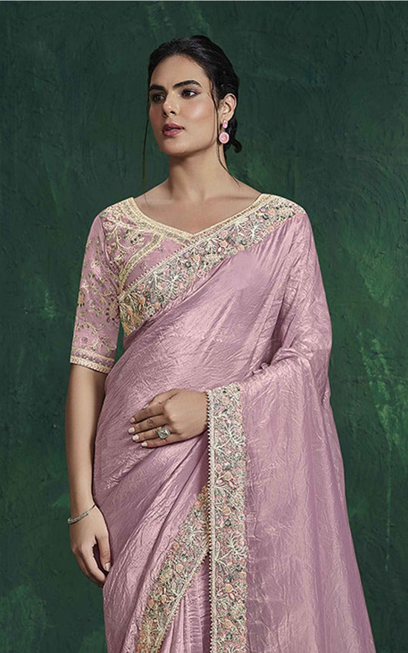 Woman wearing a pink saree with intricate designs on a green background