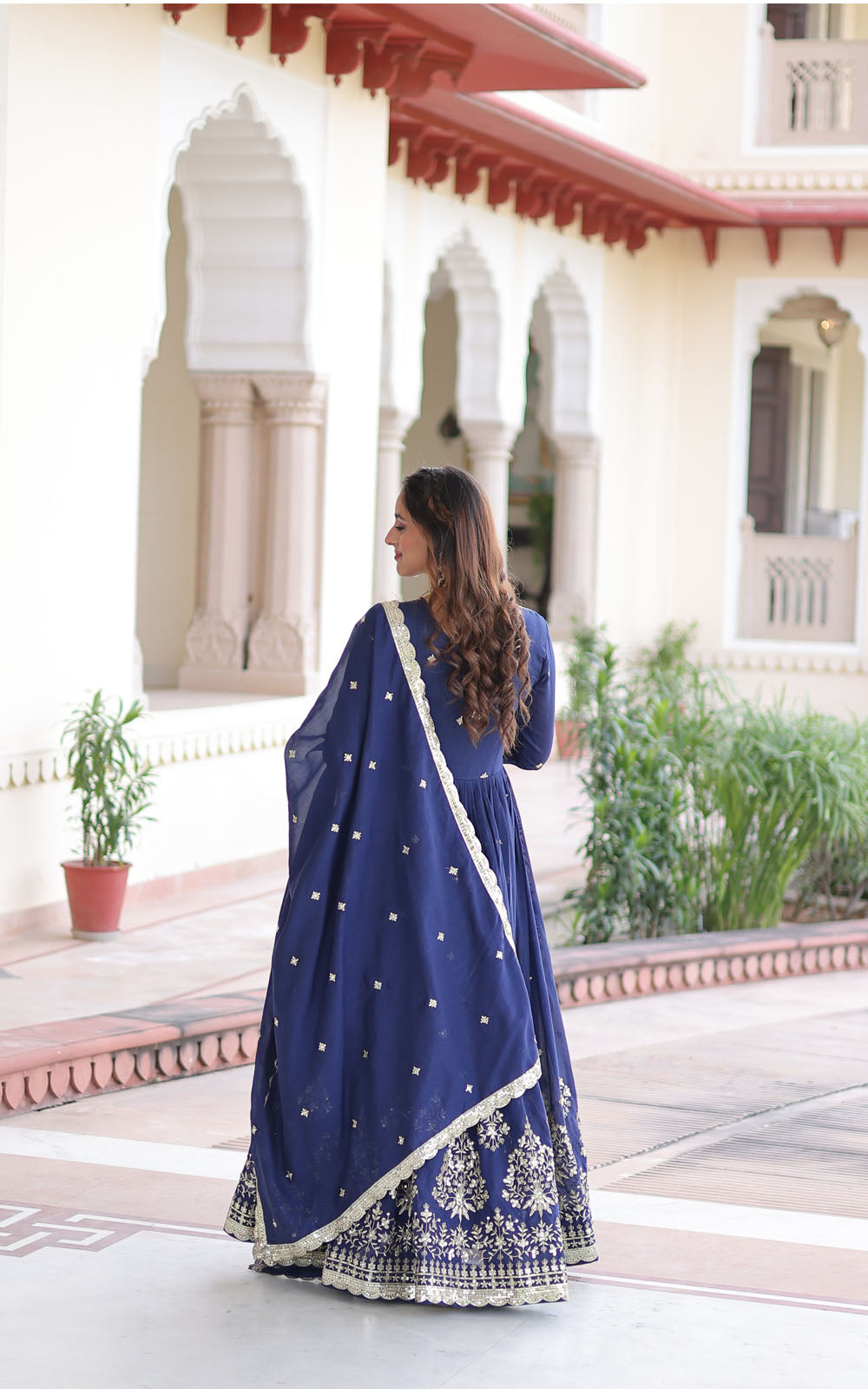 Woman in a blue traditional outfit standing in front of an architectural building.