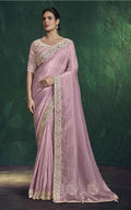 Woman wearing a pink saree with gold embroidery against a dark green background